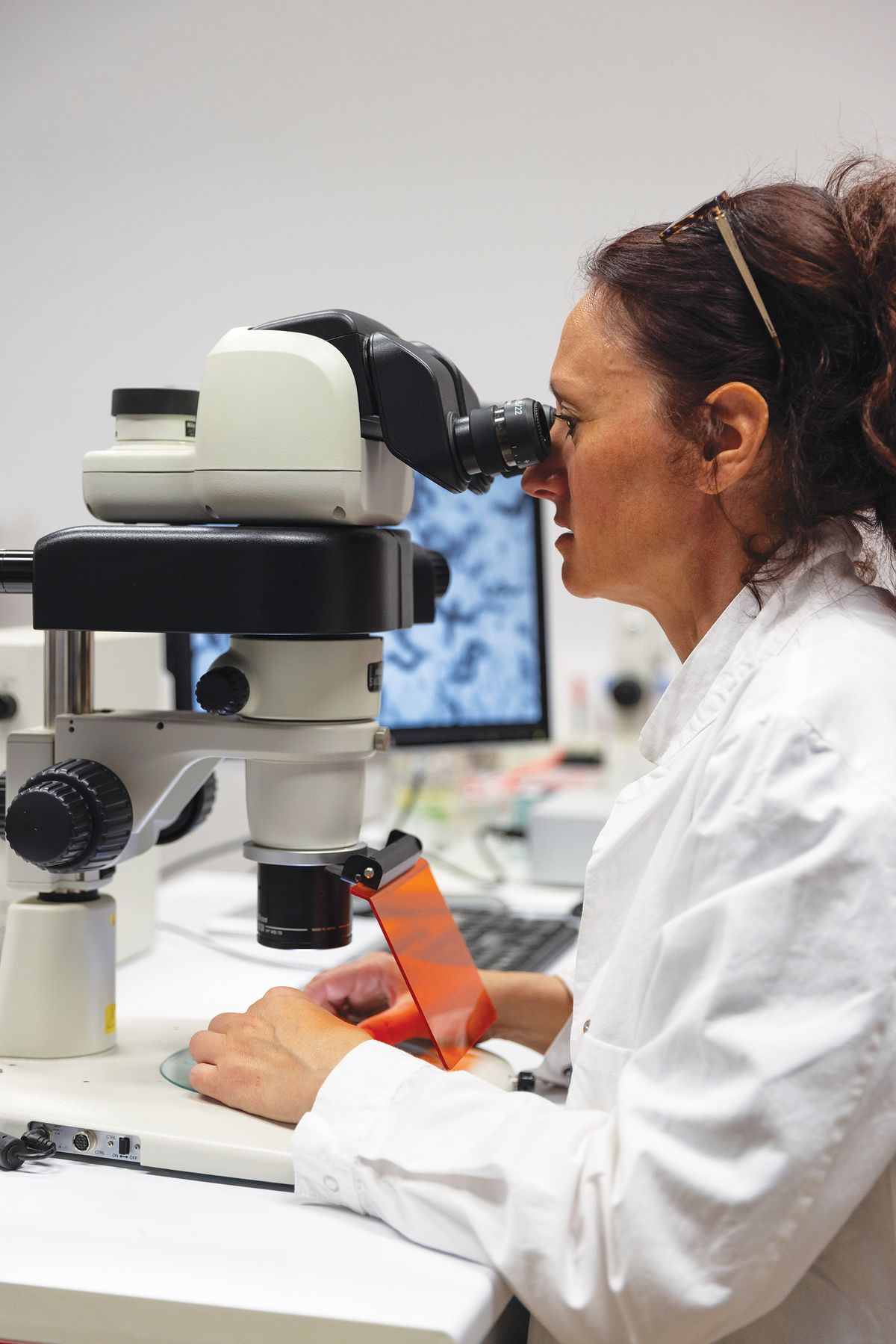 Woman in a white lab coat looking through a microscope.