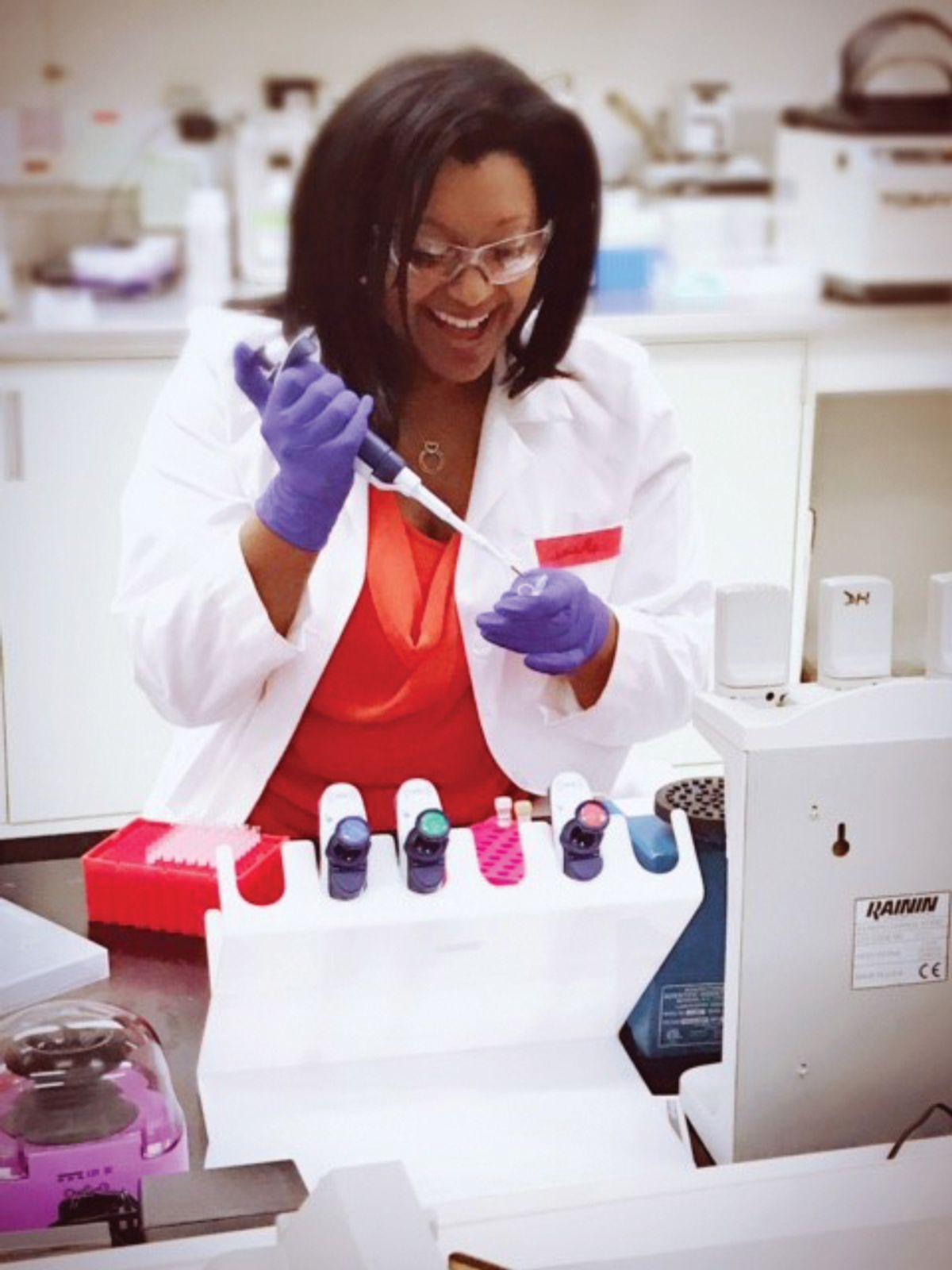 Samantha Maragh is wearing a white lab coat and holding a pipette in the lab.