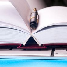 Close up image of an open notebook with blank pages, a computer keyboard, and a pen.