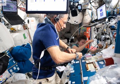 Eytan Stibbe wears a headset and a blue shirt while surrounded by computers and other equipment on the International Space Station.