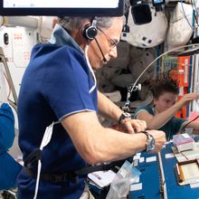 Eytan Stibbe wears a headset and a blue shirt while surrounded by computers and other equipment on the International Space Station.