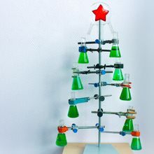 Glass laboratory flasks filled with bright green liquid arranged into a Christmas tree using a clamp stand.