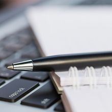 A ballpoint pen placed on top of a notebook that is sitting on top of a laptop keyboard.
